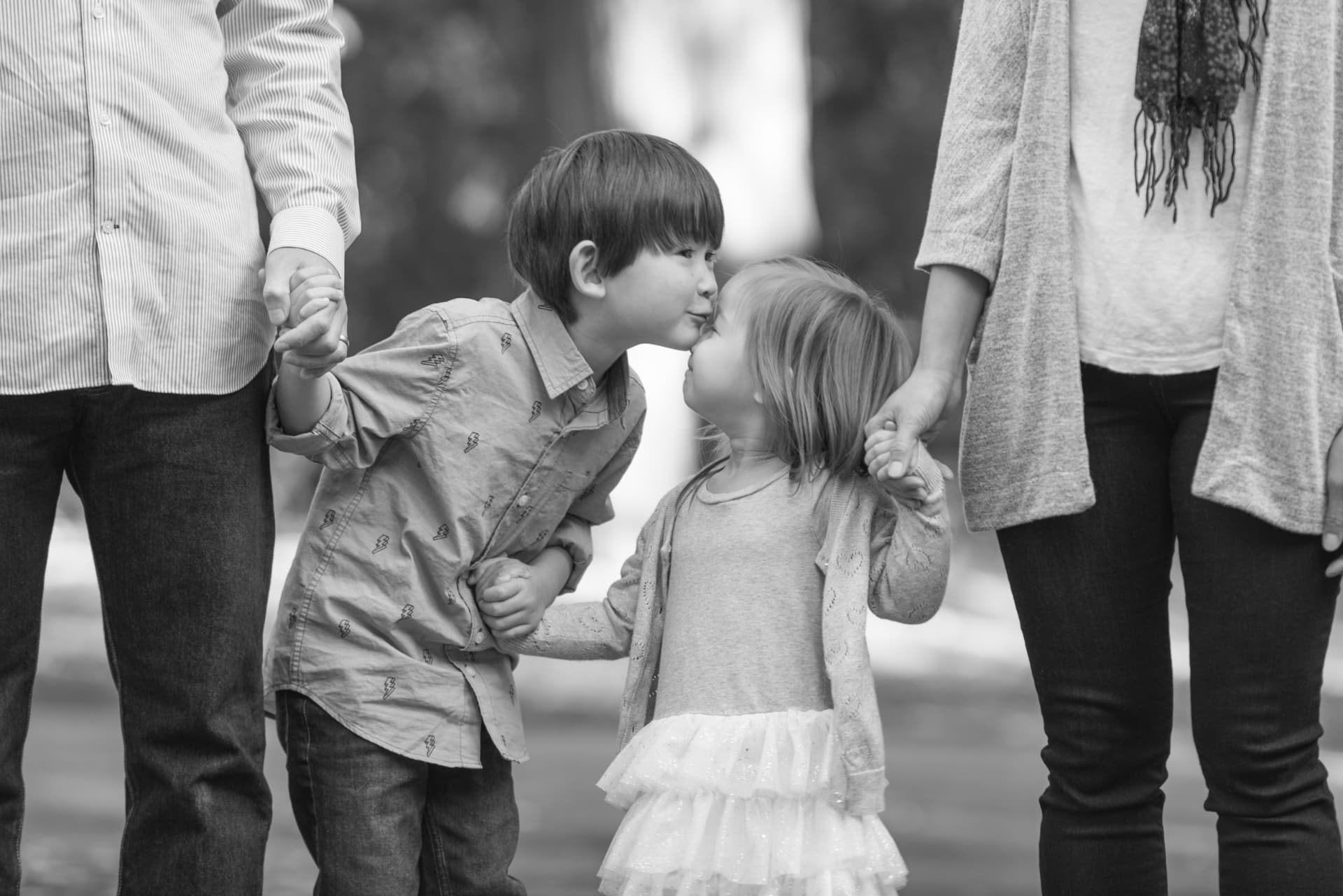 Brother and sister sharing a kiss while holding their parents' hands