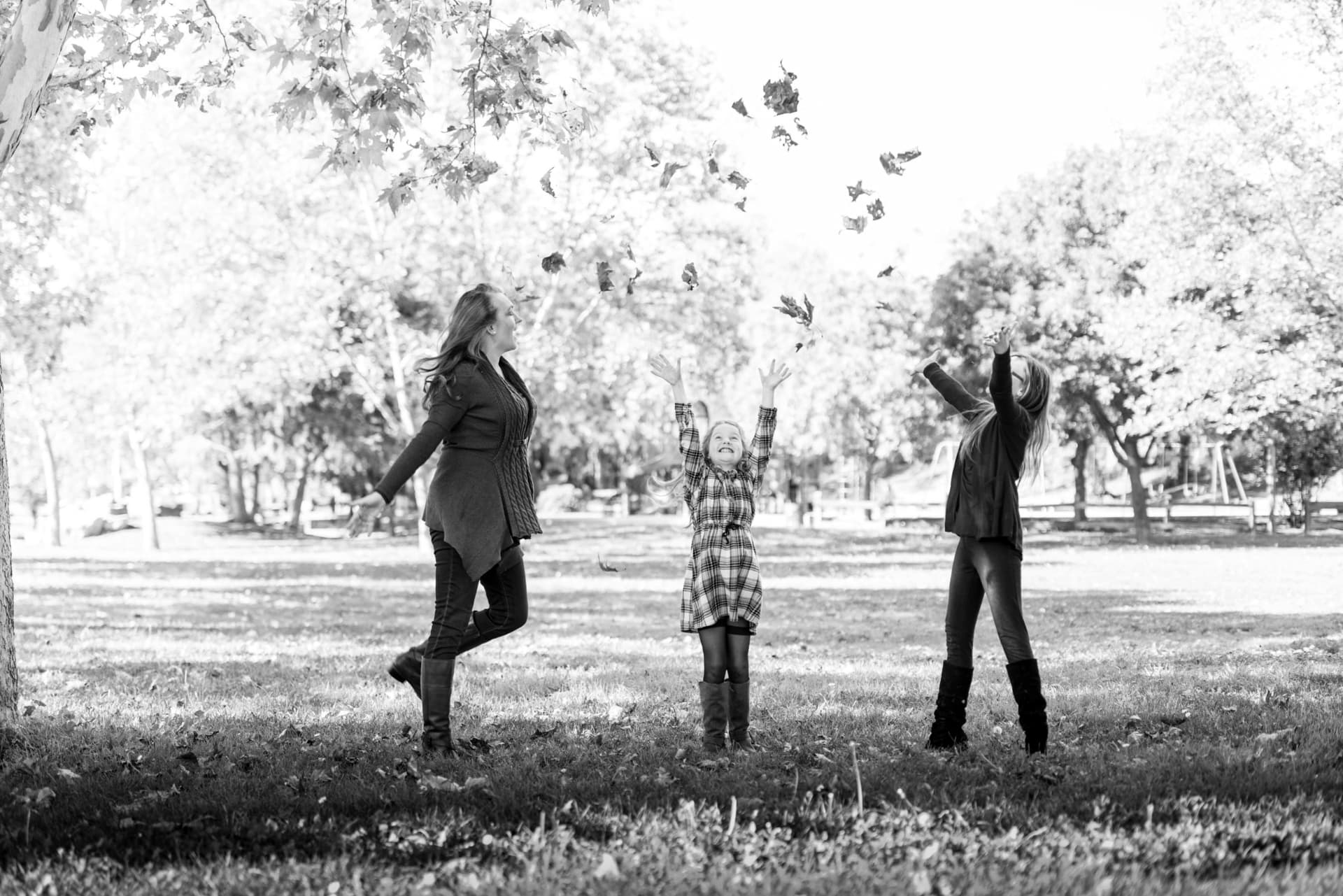 Mother and daughters tossing autumn leaves in the late afternoon light